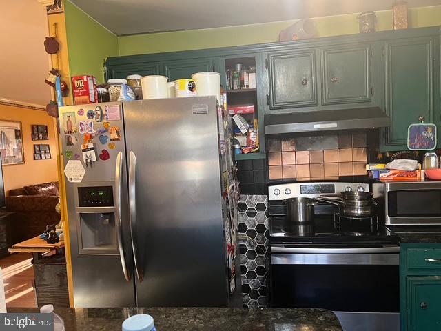 kitchen featuring stainless steel appliances, under cabinet range hood, green cabinets, dark countertops, and backsplash