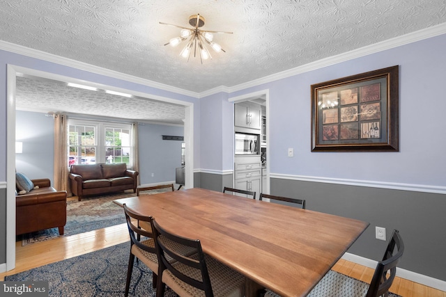 dining area with wood finished floors, a textured ceiling, a chandelier, ornamental molding, and baseboards
