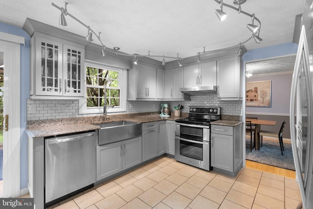 kitchen featuring appliances with stainless steel finishes, under cabinet range hood, track lighting, gray cabinetry, and a textured ceiling