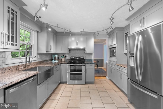 kitchen with stainless steel appliances, gray cabinets, under cabinet range hood, decorative backsplash, and a textured ceiling