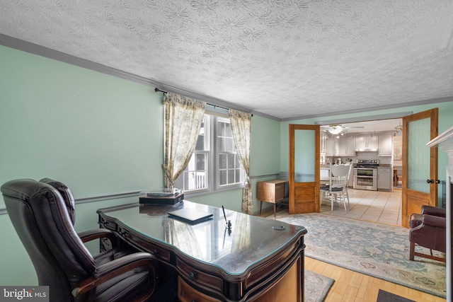 home office featuring light wood-type flooring, a textured ceiling, ornamental molding, and a ceiling fan