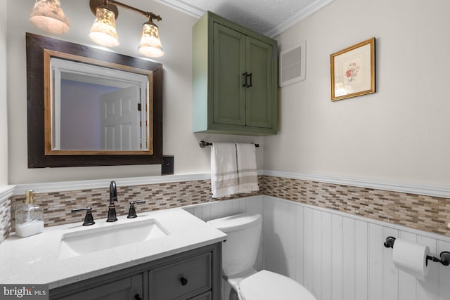 bathroom featuring a wainscoted wall, toilet, vanity, and crown molding