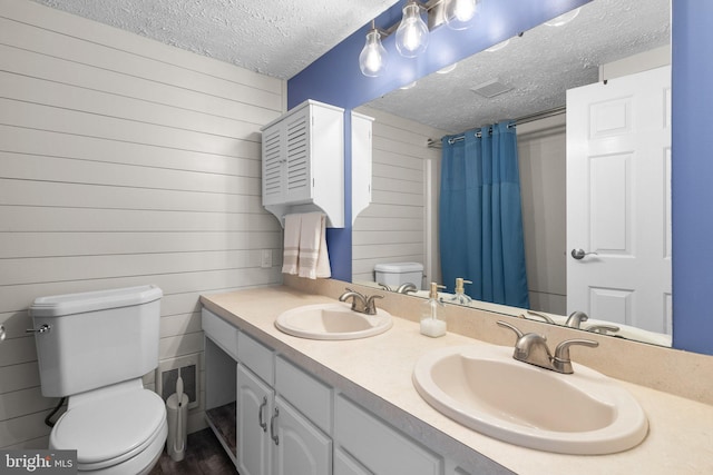 bathroom featuring toilet, a textured ceiling, wood walls, double vanity, and curtained shower