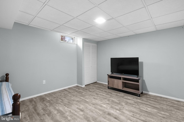 unfurnished living room featuring wood finished floors, a drop ceiling, and baseboards