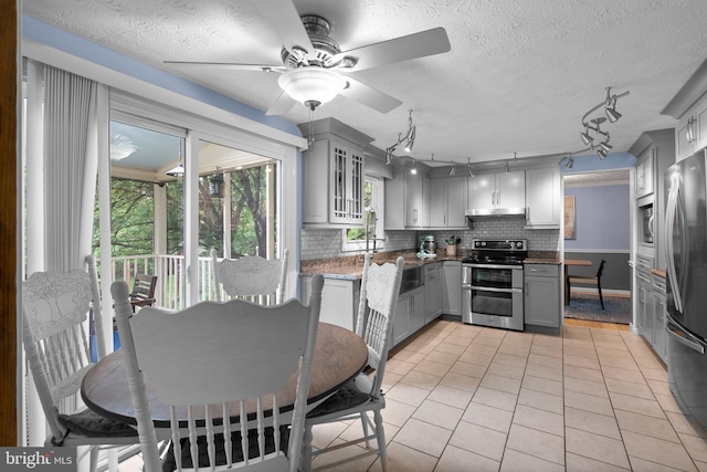 kitchen featuring appliances with stainless steel finishes, gray cabinets, light tile patterned flooring, decorative backsplash, and a ceiling fan
