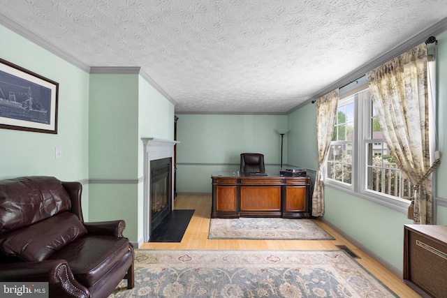office with wood finished floors, a fireplace with flush hearth, crown molding, and a textured ceiling