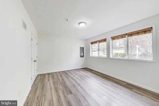 unfurnished room featuring baseboards, light wood finished floors, electric panel, and visible vents