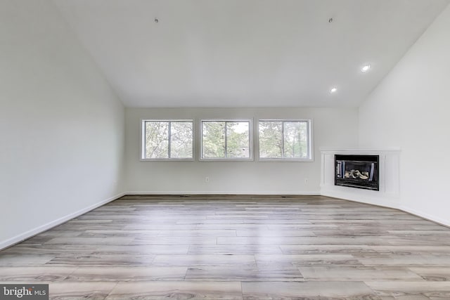 unfurnished living room featuring plenty of natural light, wood finished floors, vaulted ceiling, and a fireplace