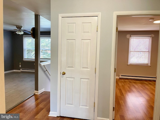 hall featuring a baseboard heating unit, plenty of natural light, baseboard heating, and wood finished floors