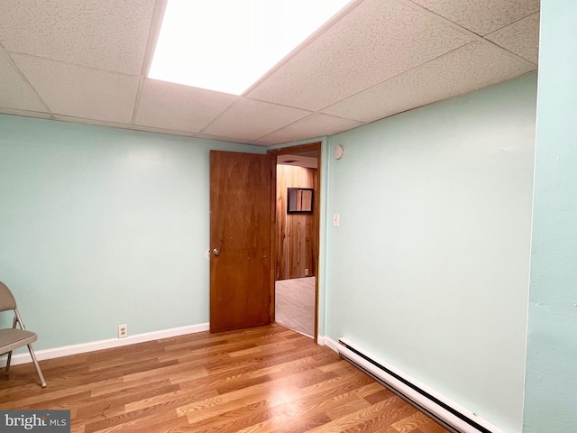 interior space featuring a baseboard heating unit, a paneled ceiling, baseboards, and light wood finished floors