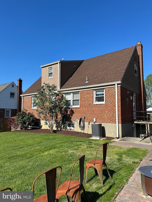 rear view of house featuring central air condition unit, a lawn, roof with shingles, and brick siding
