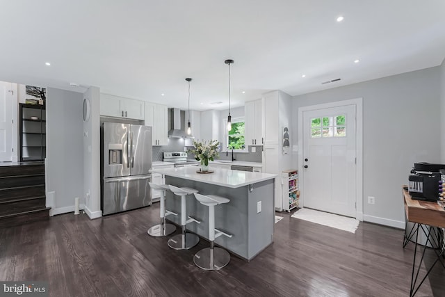 kitchen with stainless steel appliances, wall chimney exhaust hood, a sink, light countertops, and a center island