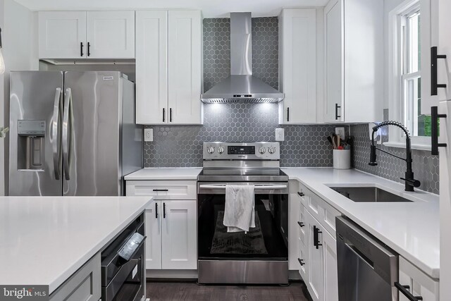 kitchen featuring appliances with stainless steel finishes, wall chimney exhaust hood, a sink, white cabinets, and light countertops