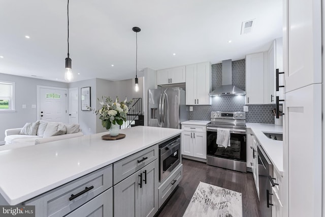 kitchen with wall chimney range hood, stainless steel appliances, dark wood finished floors, light countertops, and open floor plan