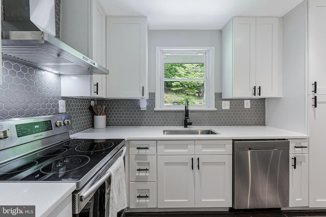 kitchen featuring stainless steel appliances, wall chimney exhaust hood, a sink, white cabinets, and light countertops
