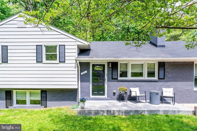 view of front of home featuring brick siding, a chimney, a front yard, and a patio