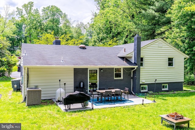 back of property featuring a chimney, an outdoor fire pit, cooling unit, a patio, and a yard