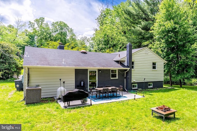 rear view of house featuring a fire pit, central air condition unit, a chimney, a patio, and a yard