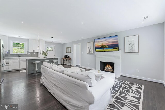 living area with a lit fireplace, dark wood-style flooring, recessed lighting, and baseboards