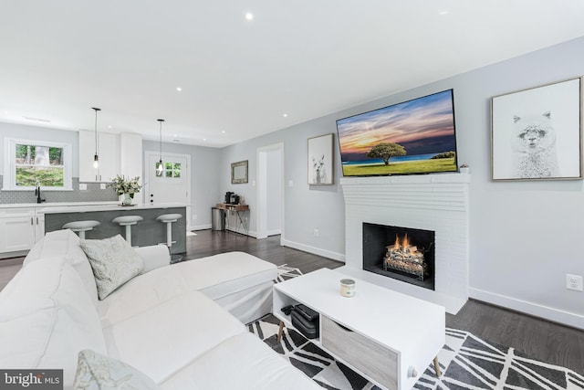 living room with dark wood-style flooring, recessed lighting, baseboards, and a warm lit fireplace