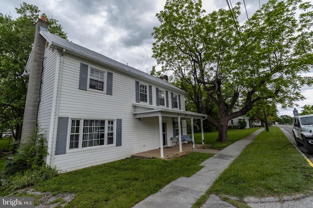 view of front of home featuring covered porch, a front lawn, and a chimney