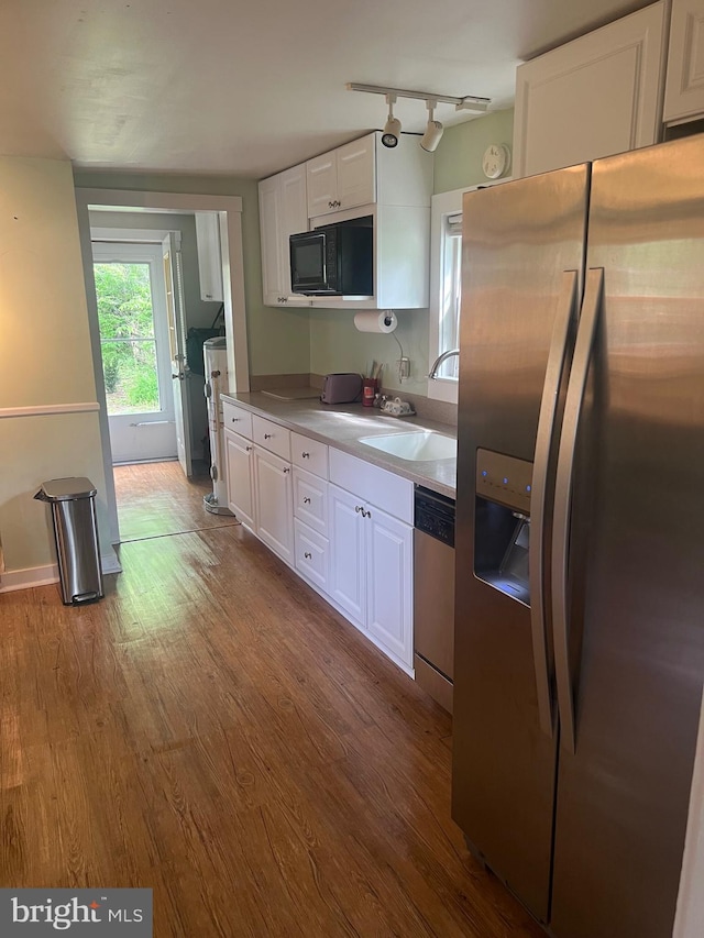 kitchen with stainless steel appliances, a sink, white cabinetry, wood finished floors, and light countertops
