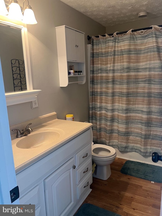 full bath featuring a textured ceiling, toilet, vanity, shower / bathtub combination with curtain, and wood finished floors