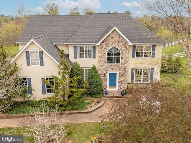 colonial house with stucco siding, stone siding, and a shingled roof