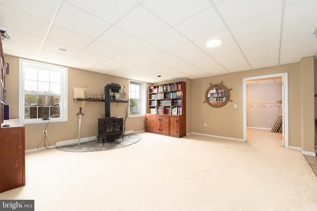 living area with carpet floors, a wood stove, a drop ceiling, and baseboards