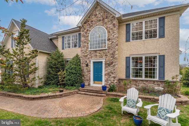 colonial house featuring stone siding, stucco siding, and a shingled roof