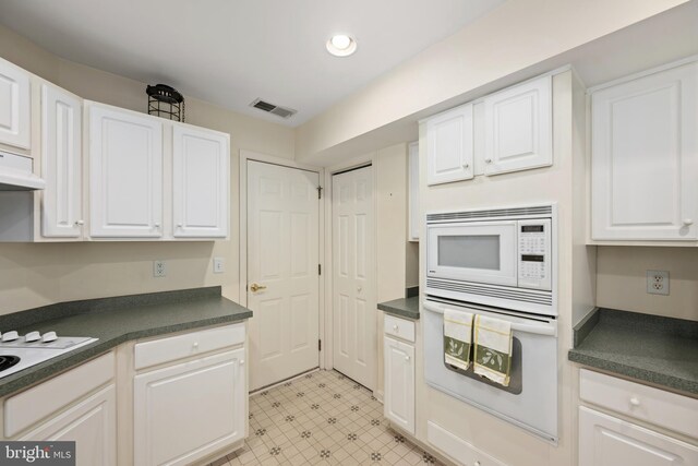 kitchen with white cabinets, dark countertops, visible vents, and white appliances