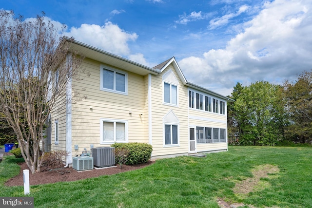 rear view of property with central air condition unit and a yard