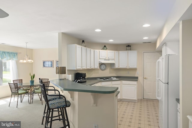 kitchen with under cabinet range hood, a breakfast bar, dark countertops, white appliances, and a peninsula