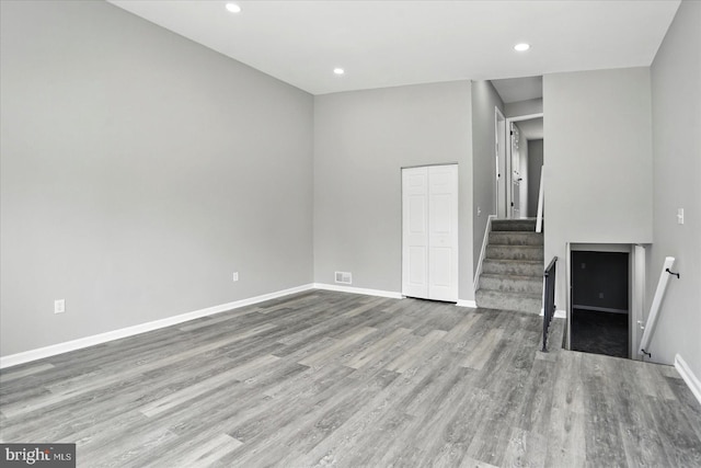 unfurnished living room featuring recessed lighting, stairs, wood finished floors, and baseboards