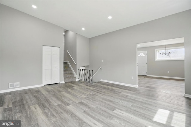 empty room with light wood-style floors, visible vents, and a notable chandelier
