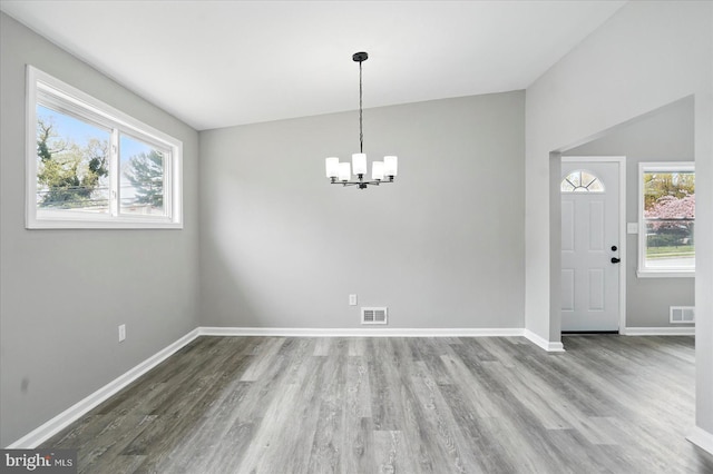 unfurnished dining area with baseboards, a notable chandelier, wood finished floors, and visible vents
