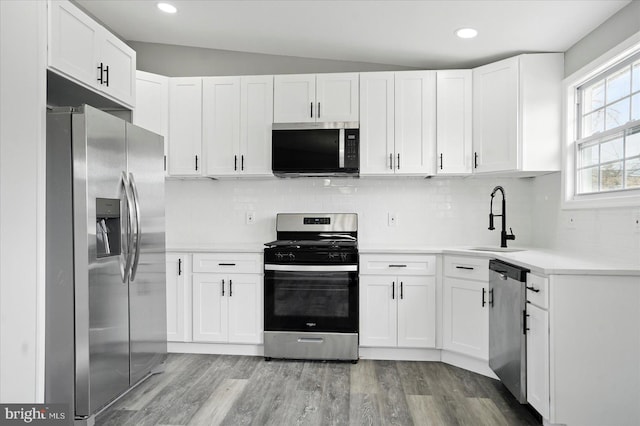 kitchen featuring white cabinetry, stainless steel appliances, light wood finished floors, and a sink