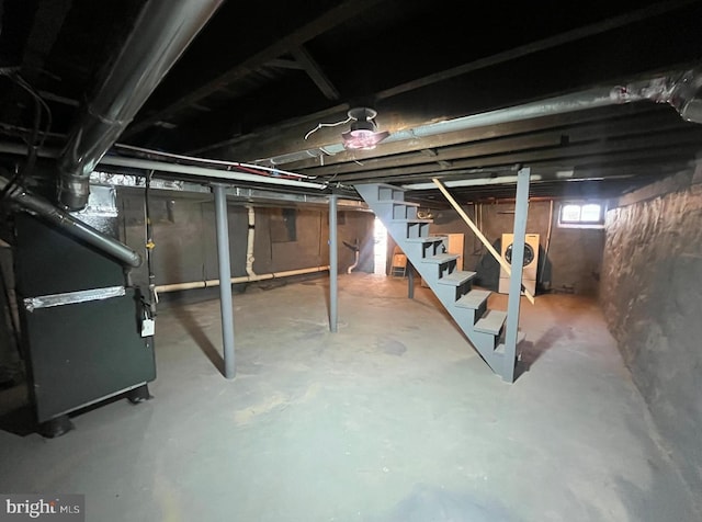 below grade area featuring washing machine and clothes dryer, heating unit, and stairway