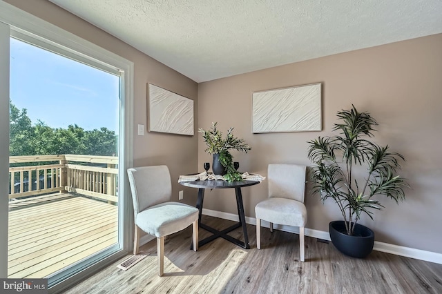 sitting room with a textured ceiling, baseboards, visible vents, and wood finished floors