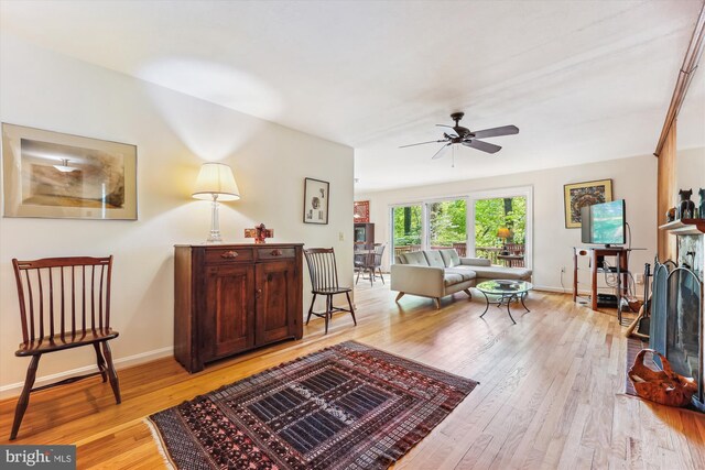 living area with light wood-style floors, a ceiling fan, and baseboards