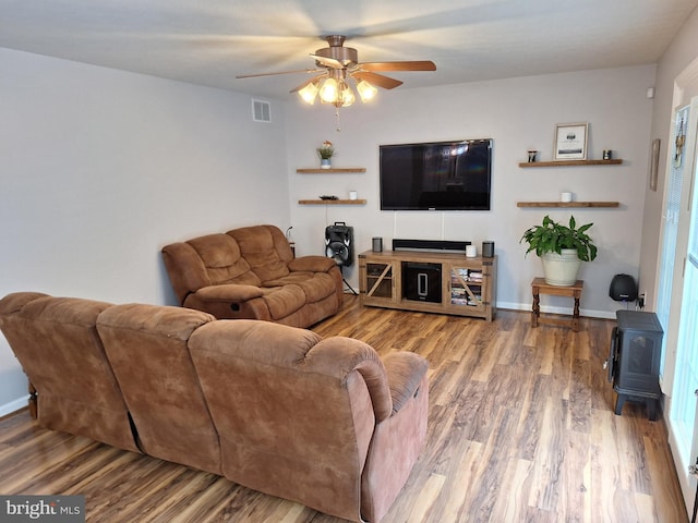 living room with ceiling fan, visible vents, wood finished floors, and a wood stove