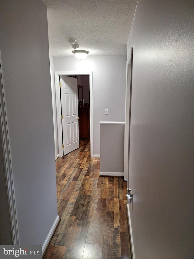 hall featuring a textured ceiling, baseboards, and hardwood / wood-style flooring