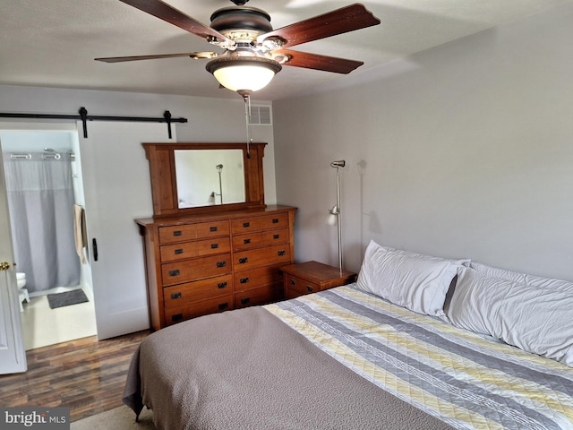 bedroom with a ceiling fan, visible vents, a barn door, and wood finished floors
