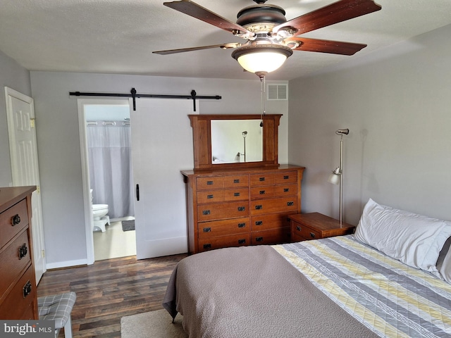 bedroom with a ceiling fan, visible vents, a barn door, dark wood-style floors, and ensuite bath