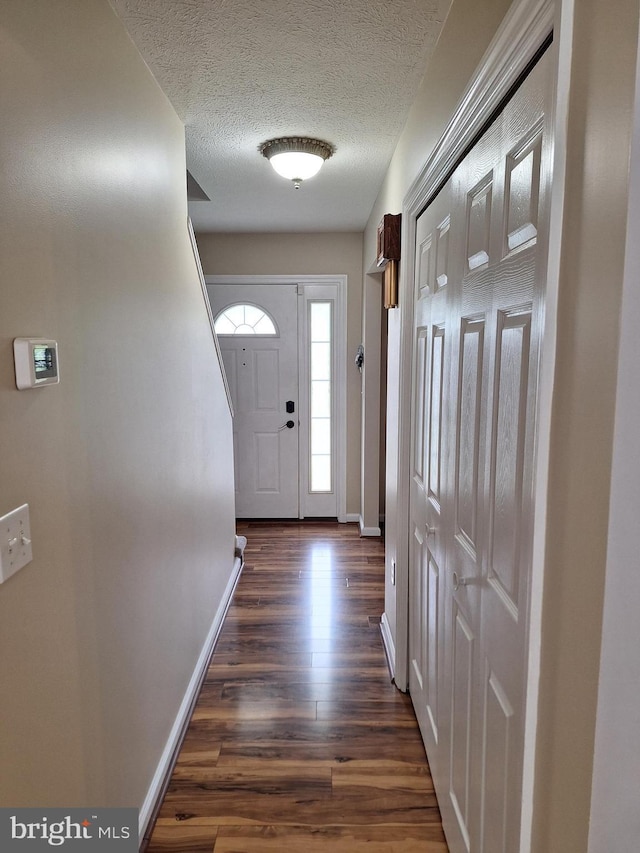 doorway to outside featuring baseboards, a textured ceiling, and dark wood-type flooring