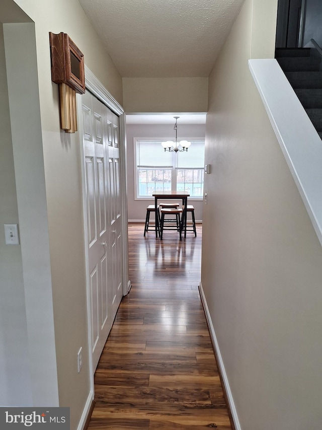 corridor featuring an inviting chandelier, dark wood finished floors, baseboards, and stairway