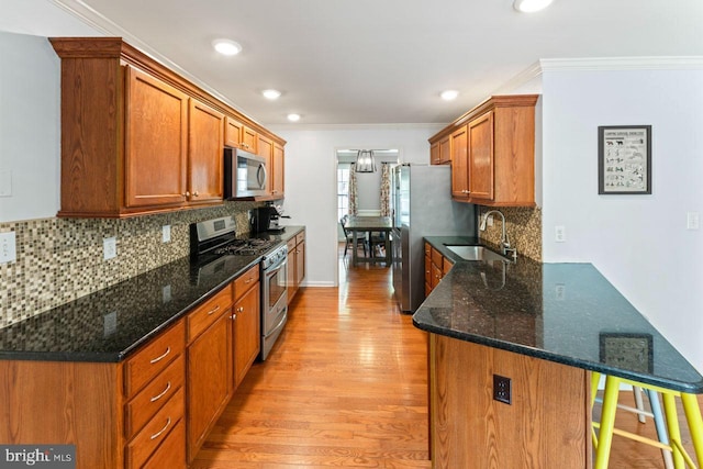 kitchen with appliances with stainless steel finishes, a sink, light wood-type flooring, a peninsula, and crown molding