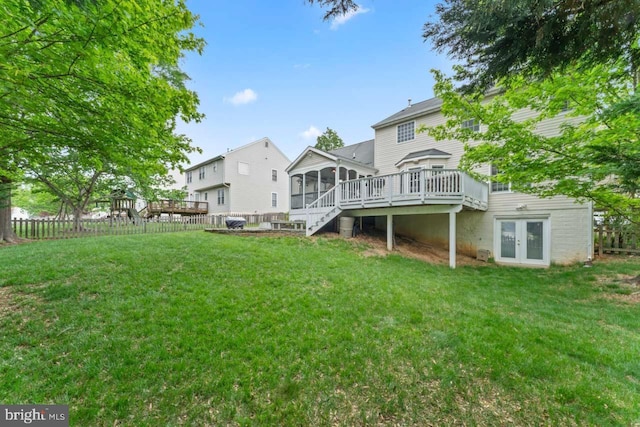 rear view of house featuring french doors, a wooden deck, a sunroom, and a lawn