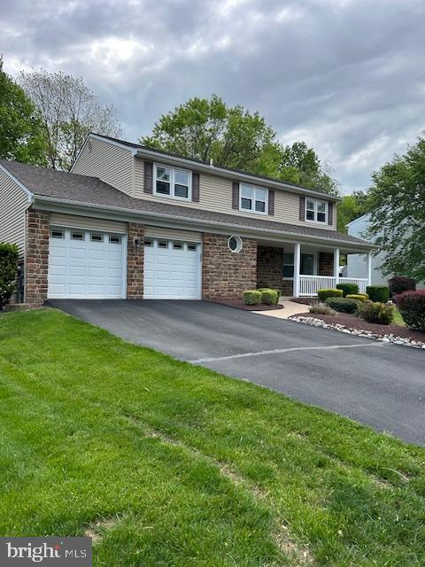 view of front of house featuring a porch, aphalt driveway, a garage, and a front yard