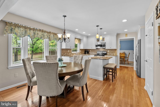 dining space featuring an inviting chandelier, light wood-style floors, a wealth of natural light, and baseboards